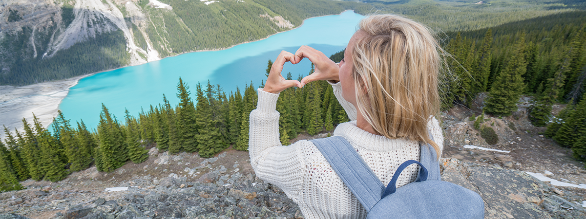 Woman making a heart with her hands on top of a hill overlooking wilderness
