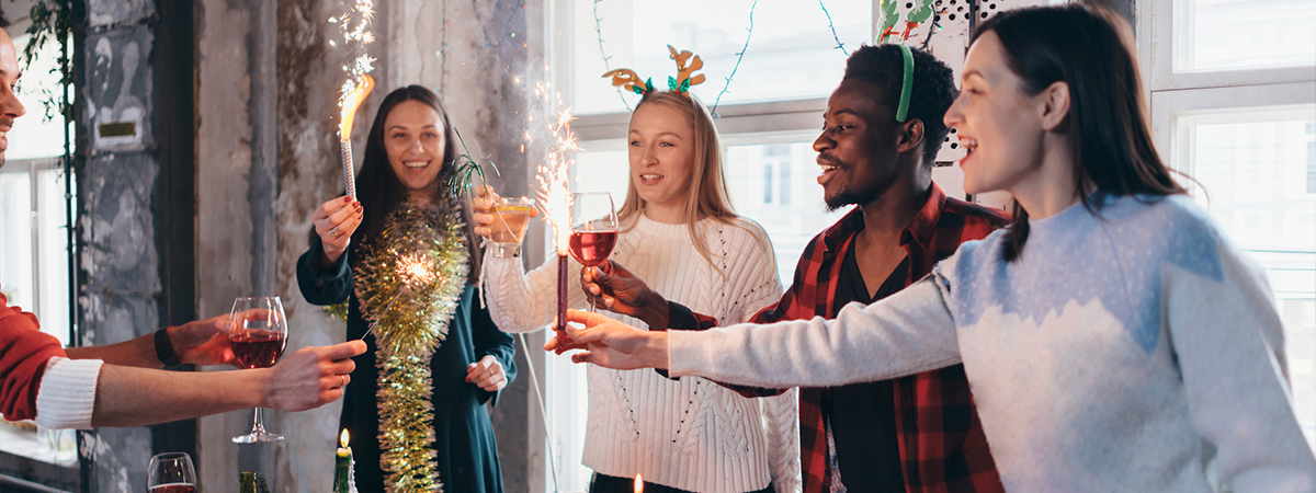 Group of people celebrating Christmas or New Year eve. Friends toasting drinks and enjoying dinner together.