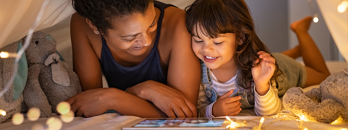 Little girl with mom watching movies on digital tablet in bedroom.