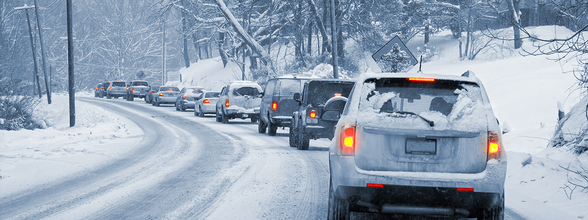 A line of cars slowly driving on a snowy, icy road.