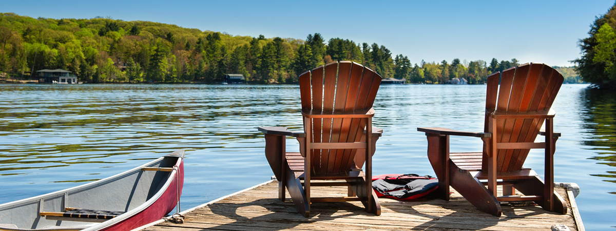 Muskoka chairs on a dock beside a canoe looking out to a lake