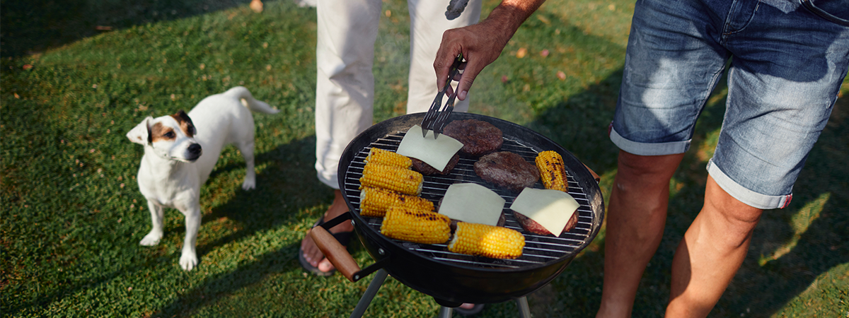 Man barbequing hamburgers and corn as his dog watches 