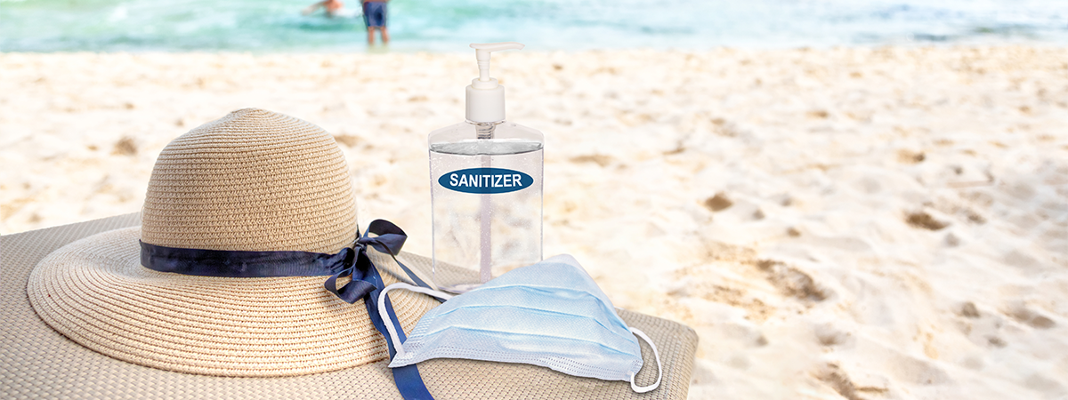 Hat, face mask and hand sanitizer on chair at the beach