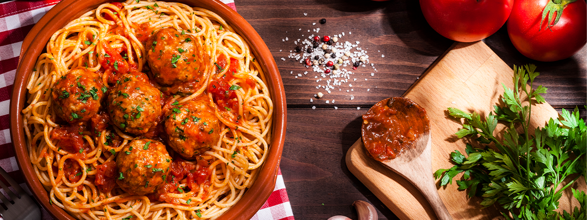 A plate of spaghetti and meatballs surrounded by cooking tools and ingredients