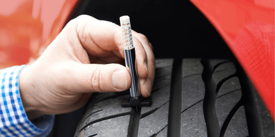 Close up of hand using tire tread depth gauge to check vehicle tire tread depth.