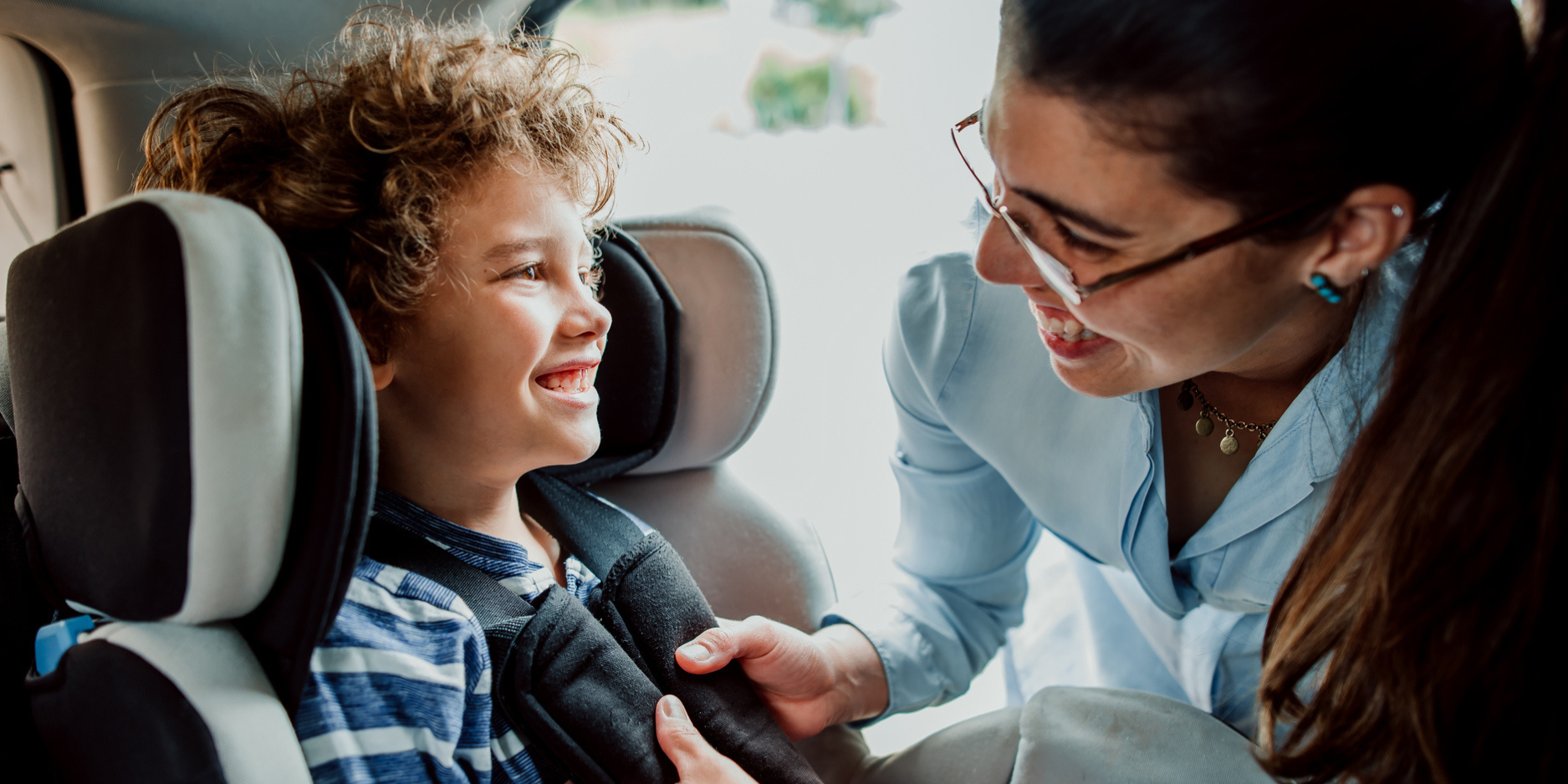 mother securing young child into carseat, both are smiling