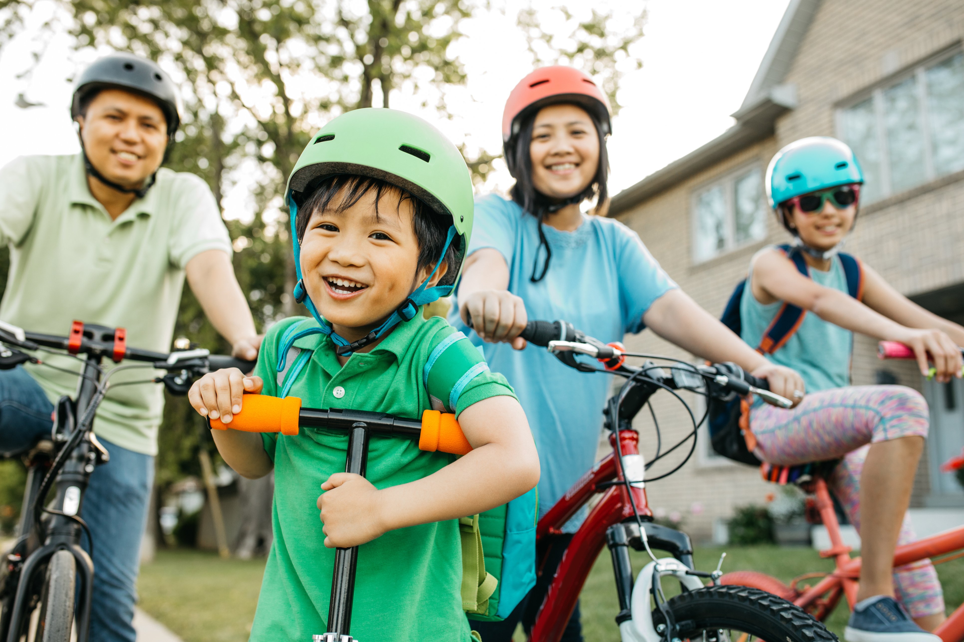 Smiling family outdoors on bikes and scooters.