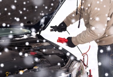 Driver using jumper cables to start dead battery in middle of winter. 