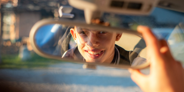 teen looking in rear-view mirror in car