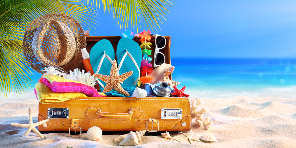 Travel items popping out of a suitcase on a tropical beach