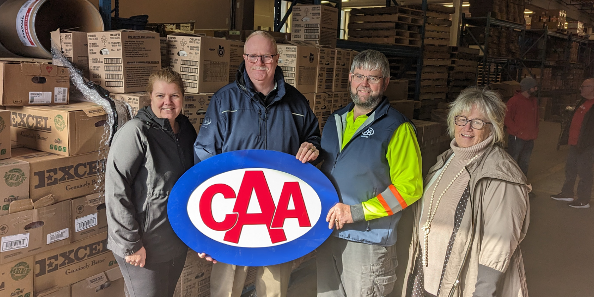 Four people pose with a CAA Niagara sign in front of boxes of donations.