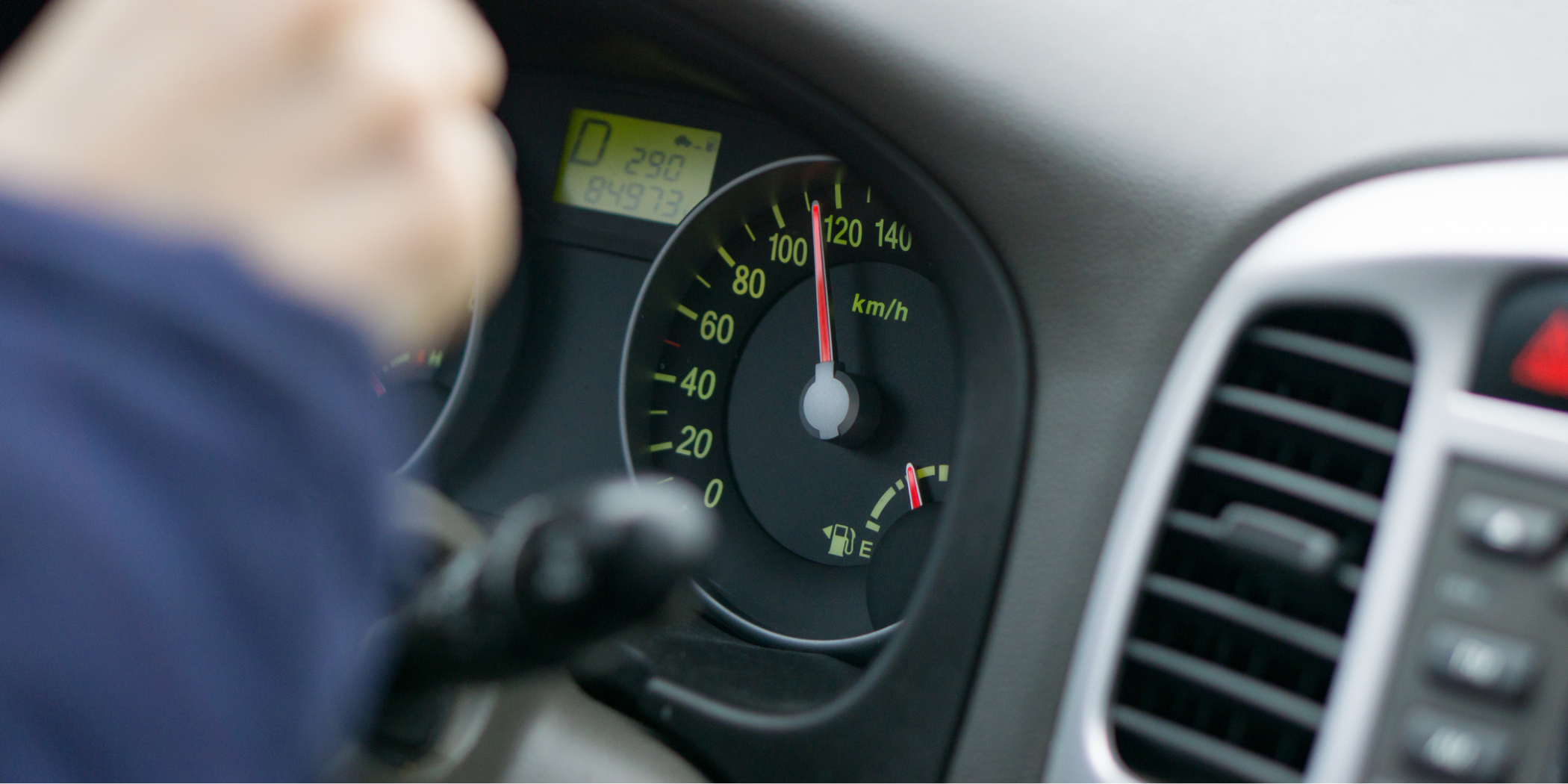 selective focus image of car interior. focus on analog speedometer - overspeeding concept. driver hands on steering wheel.