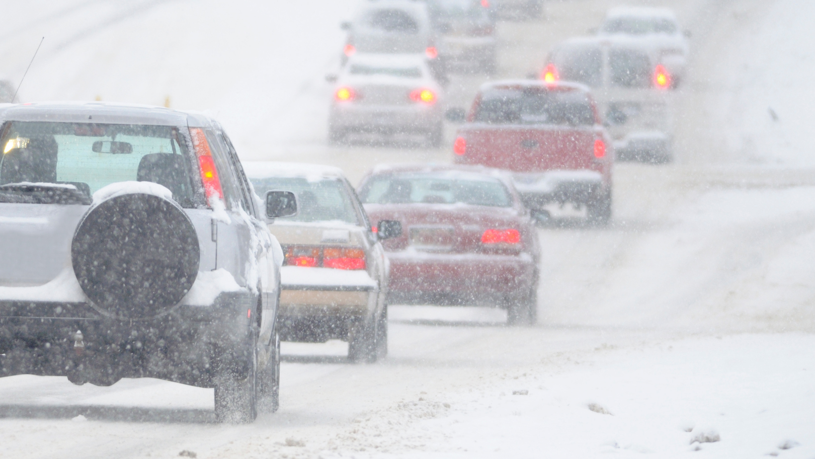 Cars driving on road in dangerous winter driving conditions.