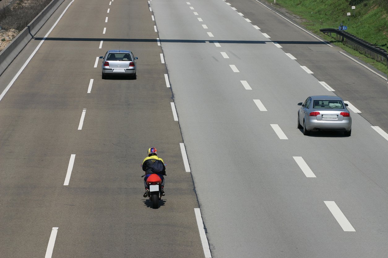 Two cars and a motorcycle on the highway, following at safe distances.